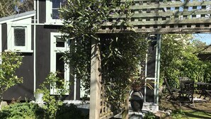 Una casa moderna con una pérgola de madera, un jardín con diversas plantas y flores, y un muro de ladrillo.