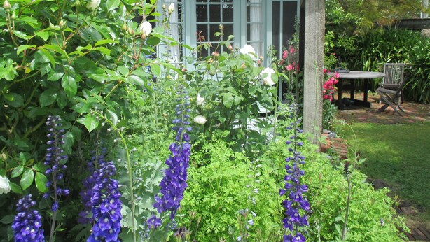Un jardín con un porche de madera, un patio de ladrillo y una mesa con sillas.