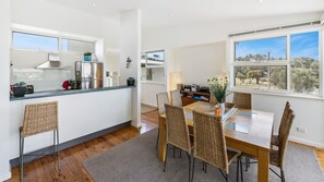 A modern kitchen with a dining area, featuring a large window, wooden flooring, and wicker chairs.