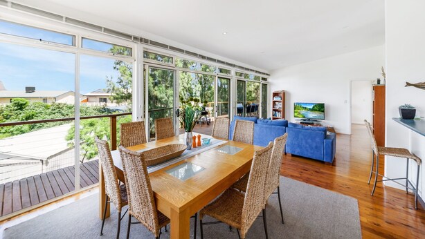 A spacious living area with a wooden dining table, wicker chairs, a blue sofa, and a television.