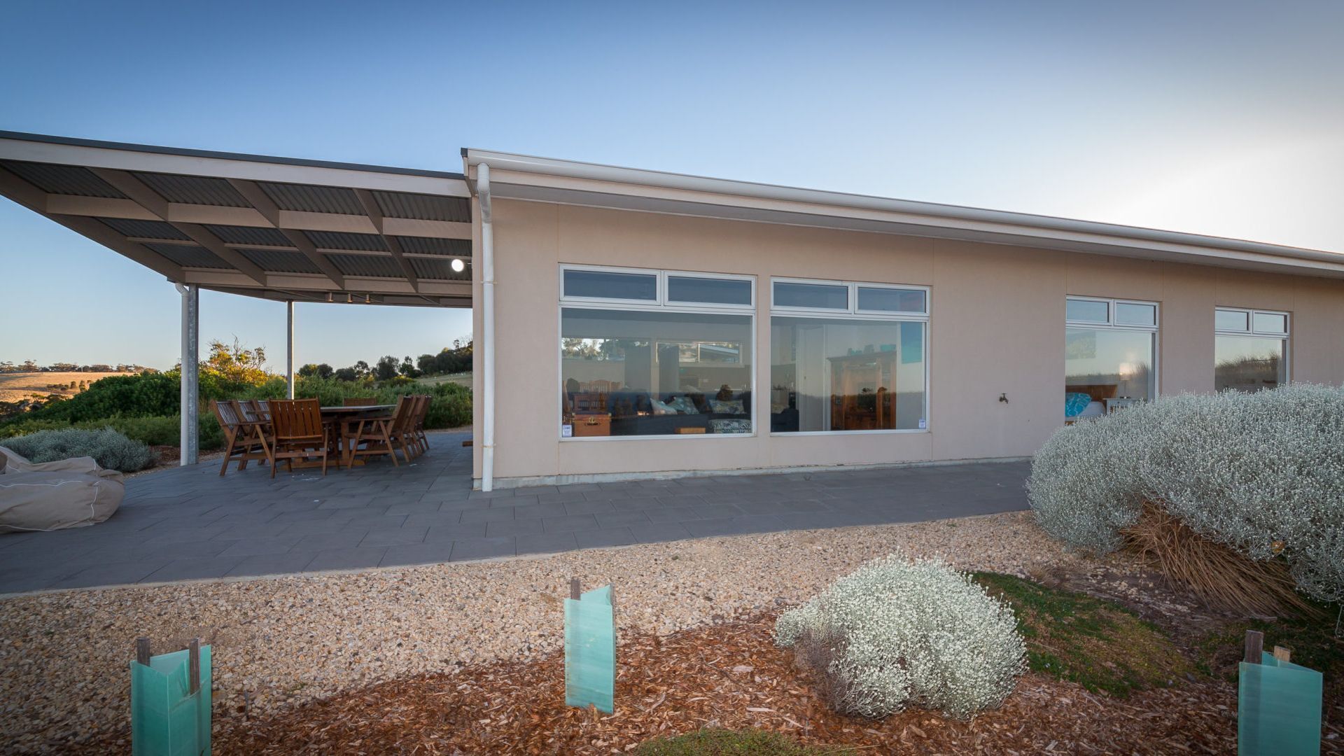 A modern house with a covered patio, large windows, and a gravel driveway.