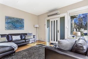 Relax in this stylish living room with a dark leather sofa, patterned cushions, and a large abstract painting.