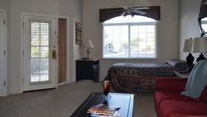 A bedroom with a bed, a red couch, a coffee table with magazines, a ceiling fan, and a window with blinds. - Luxury Studio Apartment Located in a Popular High Desert Resort (Green Valley)