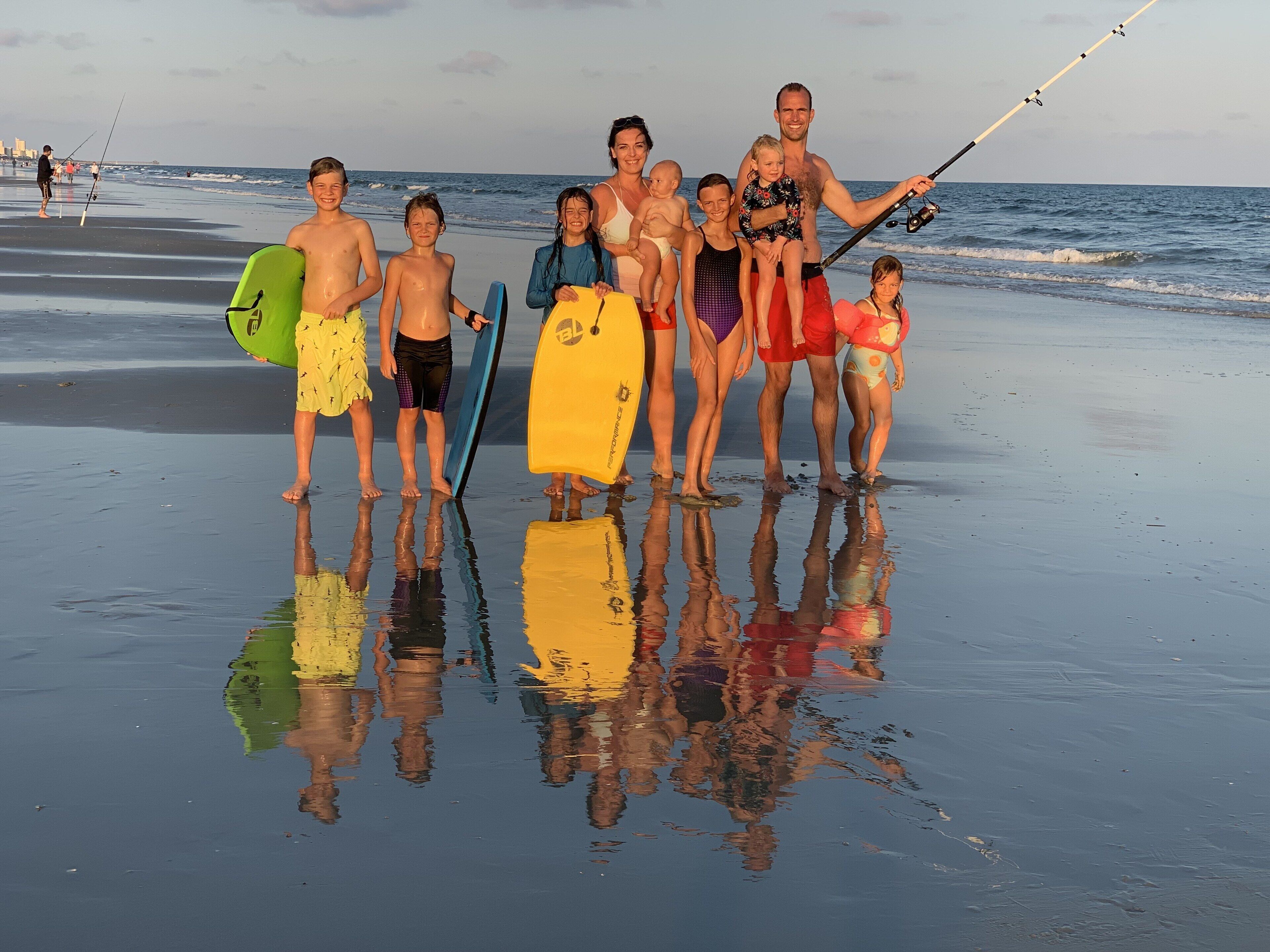 A group of people on a beach with surfboards and a fishing rod.