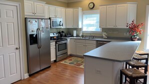 A downstairs kitchen with white cabinets, stainless steel appliances, a built-in oven, a microwave, a sink, and a small island with stools.