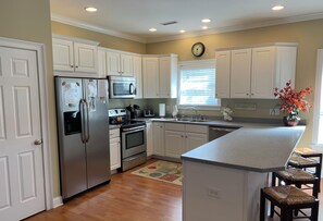 A downstairs kitchen with white cabinets, stainless steel appliances, a built-in oven, a microwave, a sink, and a small island with stools. - Spacious Luxury Beach Home, Htd. Pool, H-cap friendly, Pets, Pool Table, Golfers (North Myrtle Beach)