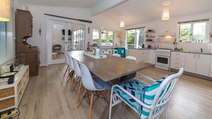 A modern kitchen with a wooden dining table, white chairs, and a view of the outdoors. - Linga Longa - 20 Laronde (CARRICKALINGA)