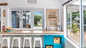 A kitchen with a wooden countertop, white bar stools, a poster, and a view of the outdoors. - Linga Longa - 20 Laronde (CARRICKALINGA)