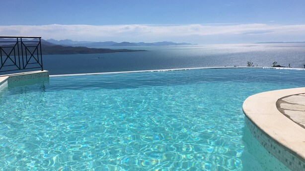 Ein Infinity-Pool mit klarem, blauem Wasser, einer gefliesten Kante und Blick auf entfernte Berge sowie ein Gewässer.