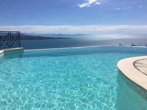 An infinity pool with clear blue water, a tiled edge, and a view of distant mountains and a body of water. - Prestige Villas | AGNI | 5* Balinese Style VilIa with Pool & Views Over Agni (Kentroma Corfu)