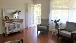 A spacious room with hardwood flooring, a white cabinet with glass doors, a comfortable armchair, a small table, and a potted plant. - Sawtells Cozy cottage (Sawtell)
