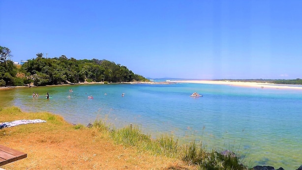 A coastal beach with clear waters, a sandy beach, and a boat in the distance. - Sawtells Cozy cottage (Sawtell)