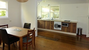 A kitchen with wooden cabinets, a sink, and a stove. There is a dining table with chairs and a hanging light fixture. - Sawtells Cozy cottage (Sawtell)