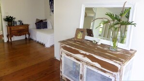 A room with a wooden dresser, a bed with patterned bedding, a small table with a plant, and a mirror reflecting the room. - Sawtells Cozy cottage (Sawtell)