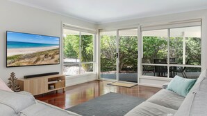 Un salon moderne avec un grand téléviseur, un canapé et un coin repas avec des chaises.