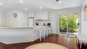 Une cuisine moderne avec des meubles blancs, un îlot central intégré doté de tabourets, et une grande porte-fenêtre coulissante donnant sur un espace extérieur.