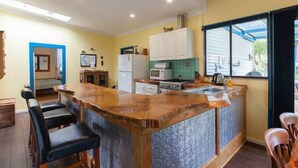 A kitchen with a central island, bar stools, a microwave, a refrigerator, and a window with a view. - Fremantle South Beach House + Outdoor Studio 4x2 (South Fremantle)