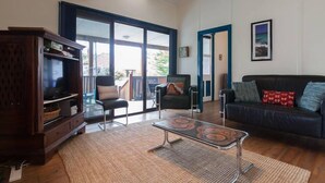 A living room with a wooden cabinet, a glass coffee table, a black sofa, and a large sliding glass door leading to an outdoor area. - Fremantle South Beach House + Outdoor Studio 4x2 (South Fremantle)