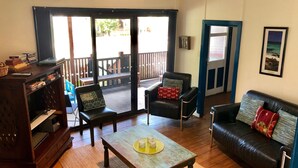 A cozy living room with a wooden coffee table, a leather sofa, and a chair with cushions. A bookshelf and an air conditioning unit are also visible. - Fremantle South Beach House + Outdoor Studio 4x2 (South Fremantle)
