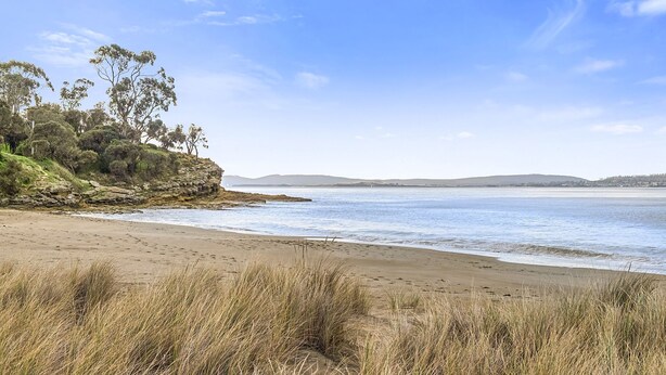 A beach with grassy dunes, a rocky outcrop, and a calm sea. - Apartments at the beach (Blackmans Bay)
