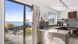 A modern kitchen with a view of the sea, a dining area with a table and chairs, and a small balcony. - Apartments at the beach (Blackmans Bay)