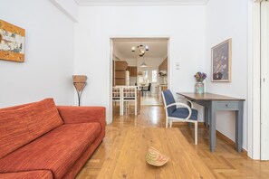 A living room with a red sofa, a wooden coffee table, and a blue chair. There is a dining area with a table and chairs in the background.