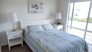 Une chambre à coucher comprenant un lit, deux tables de chevet, une commode, une œuvre d’art accrochée au mur et une fenêtre donnant sur un paysage.