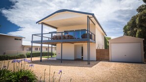 Une maison à deux étages avec un balcon, un garage et une allée gravillonnée.