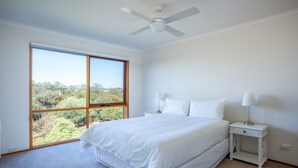 Quarto com uma janela grande, uma cama, uma mesa de cabeceira e um ventilador de teto.
