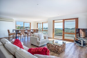 Uma sala de estar ampla com um sofá, uma mesa de centro de vidro e um espaço de jantar com cadeiras de vime.