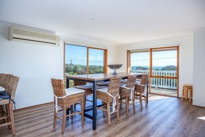 A dining area with a wooden table and wicker chairs, large windows with a view of the sea, and a balcony with a railing. - BAYSIDE BLISS | BEACH & SPECTACULAR VIEWS | SLEEPS UP TO 12 | RYE (Rye)