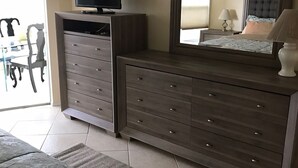 A bedroom with a bed, a dresser, a television, and a large mirror. - First Lido - New pool deck, and landscaping, 
New elevator, Freshly painted (Sarasota)