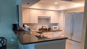 A modern kitchen with white cabinets, a built-in microwave, a stainless steel kettle, and a white refrigerator. - First Lido - New pool deck, and landscaping, 
New elevator, Freshly painted (Sarasota)
