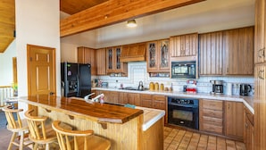 A kitchen with wooden cabinets, a central island with bar stools, a refrigerator, a stove, and a dishwasher.