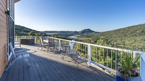 A wooden deck with outdoor furniture, a white railing, and a view of a mountainous landscape.