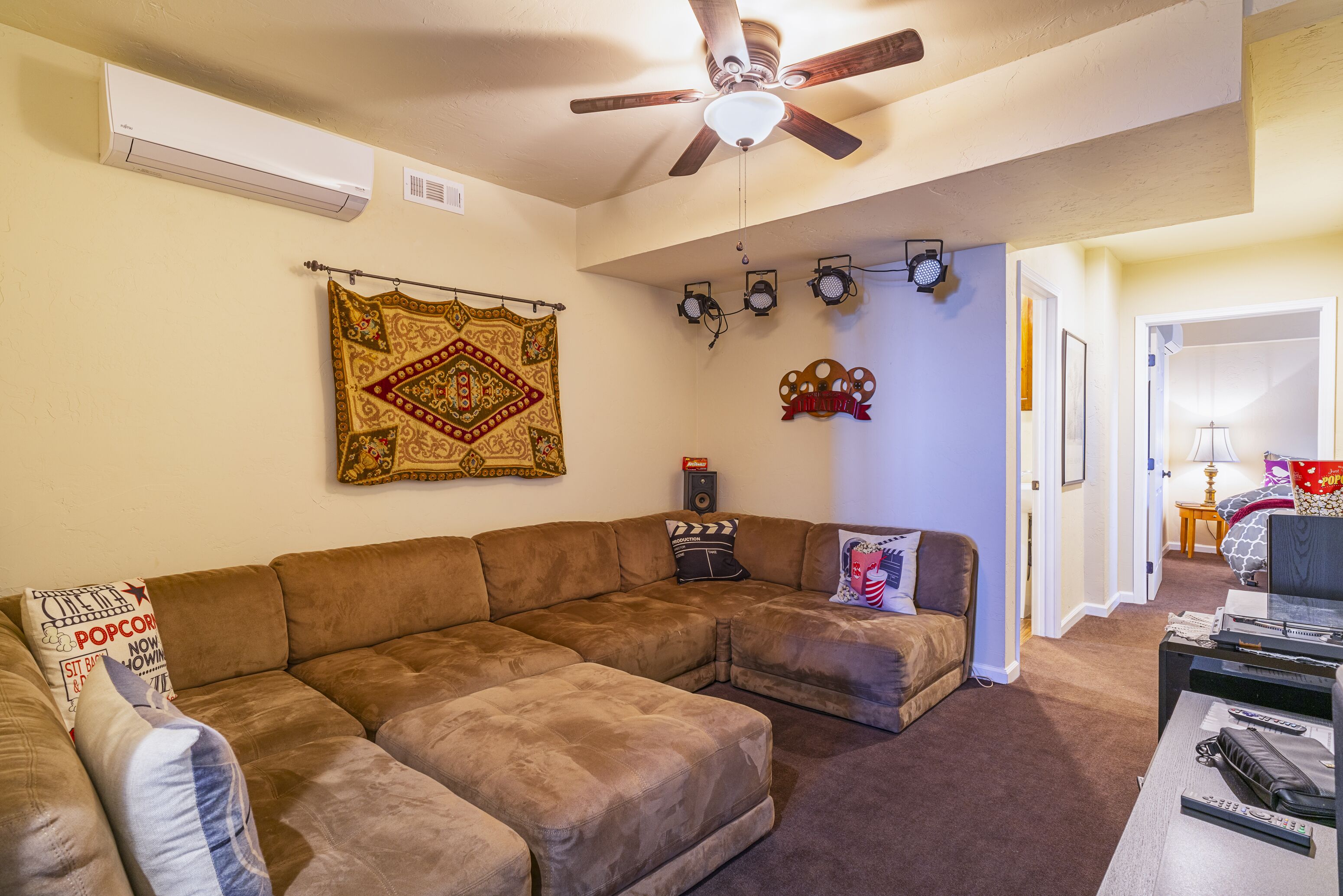 A living room with a sectional sofa, a ceiling fan, wall-mounted lights, and a patterned tapestry.