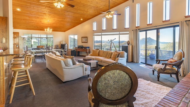 A spacious living area with a high ceiling, wooden beams, and large windows offering a view of the mountains.