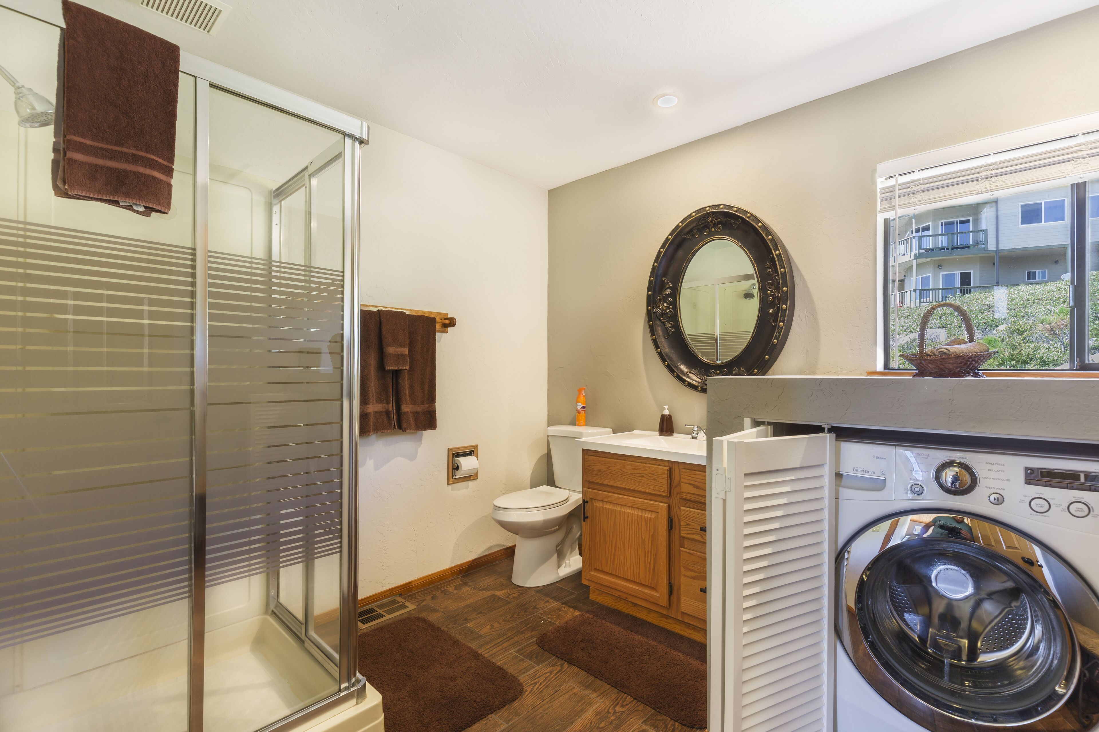 A bathroom with a glass shower enclosure, a toilet, a sink with a mirror, and a washing machine.