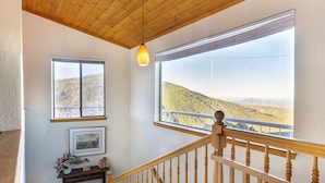 A staircase with wooden railings, a wooden ceiling, and large windows offering a view of a hilly landscape.