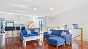 A spacious living area with a modern kitchen, a dining area with bar stools, and a balcony with a wooden railing.