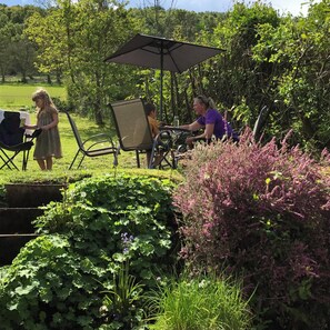 Relax in a serene garden setting with a table and chairs under a spacious umbrella, surrounded by lush greenery and vibrant flowers.