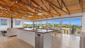 Een ruime keuken met een centraal eiland, grote ramen met uitzicht op het landschap en een hoog plafond met zichtbare houten balken.