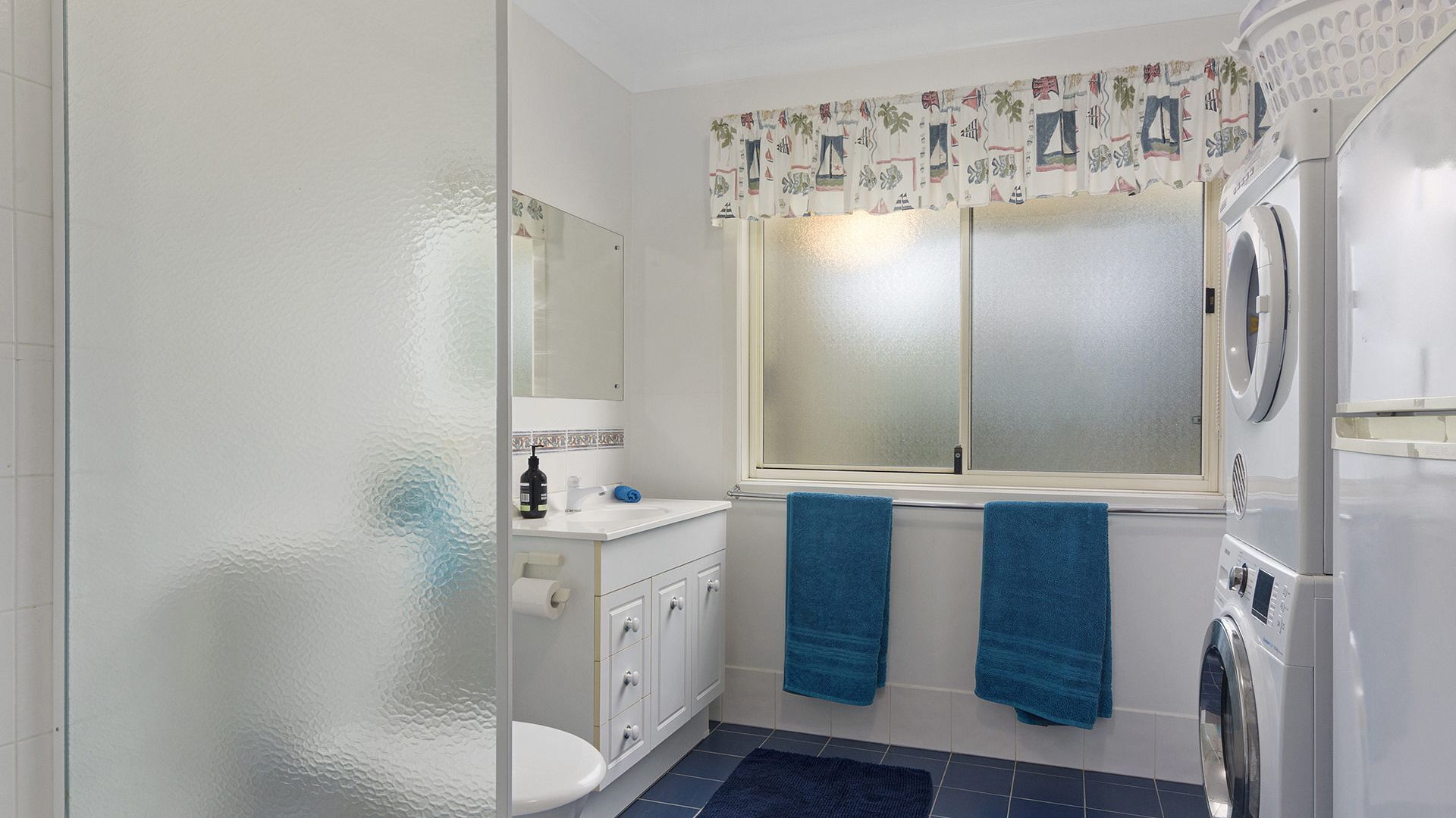 A bathroom with a washing machine, a toilet, a sink, and a window with curtains.