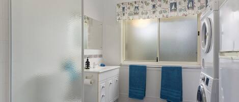 A bathroom with a washing machine, a toilet, a sink, and a window with curtains.