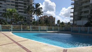 Une piscine dotée d’une terrasse carrelée, entourée d’une clôture et de palmiers.