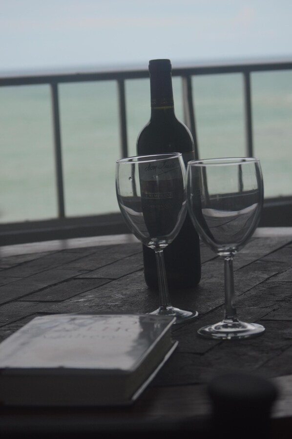 A bottle of wine and two empty wine glasses on a wooden table with a view of the ocean.