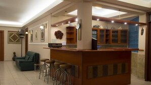 A lobby with a reception desk, bar stools, a sofa, and a clock on the wall. - One of the biggest Villas Near Athens Greece 40% off January 1 to May 15 (ANAVISSOS)