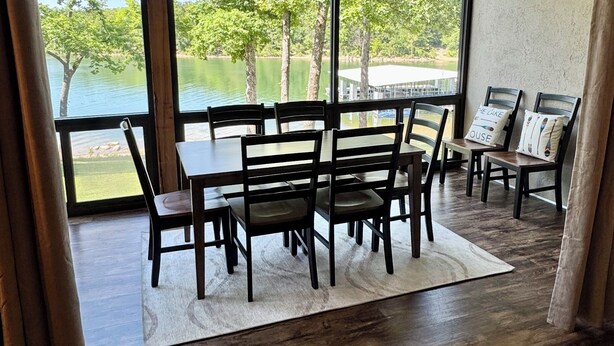 A dining area with a table and chairs, a ceiling fan, and large windows overlooking a lake. - 3 BR, 3 Bth, Vickery Resort Lower level with walkout to the lake. (Hollister)
