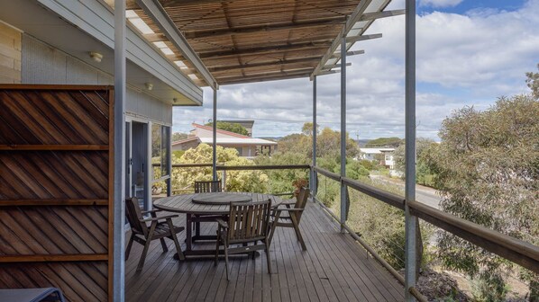 A wooden deck with a table and chairs, overlooking a residential area with houses and trees.