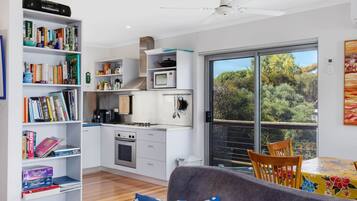 A compact kitchen with a microwave, stove, and coffee maker, alongside a bookshelf filled with books.